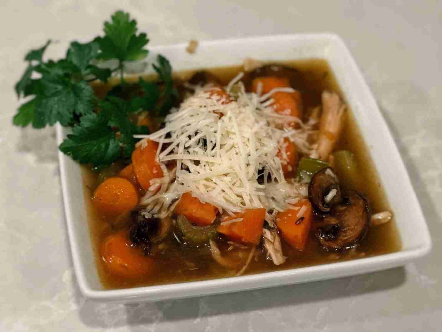Rooster wild rice soup in a square white bowl topped with fresh parsley