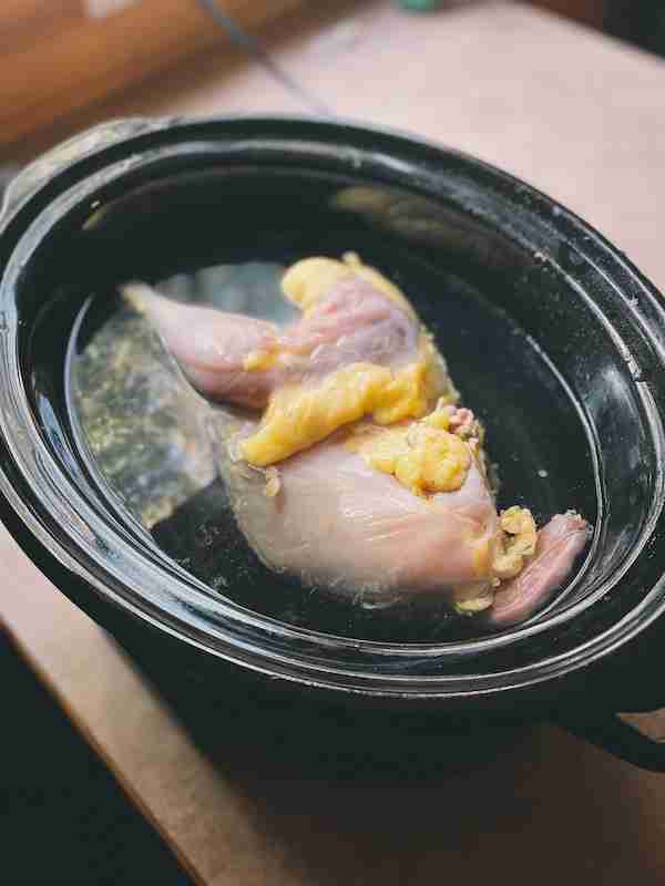 A rooster in a crockpot filled with water ready to be cooked