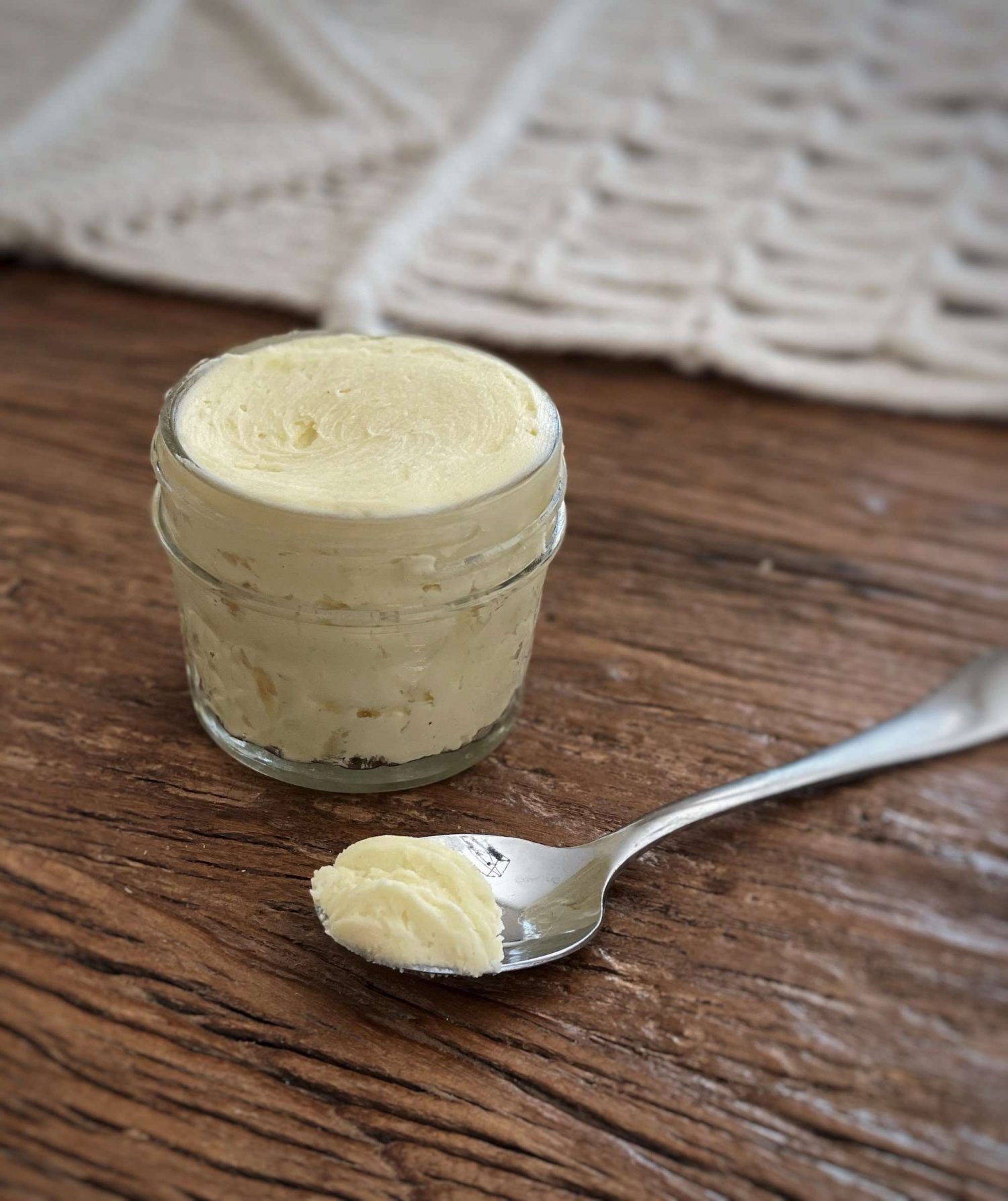 4oz jar of whipped tallow balm sitting on a wooden table with a spoonful in front of it