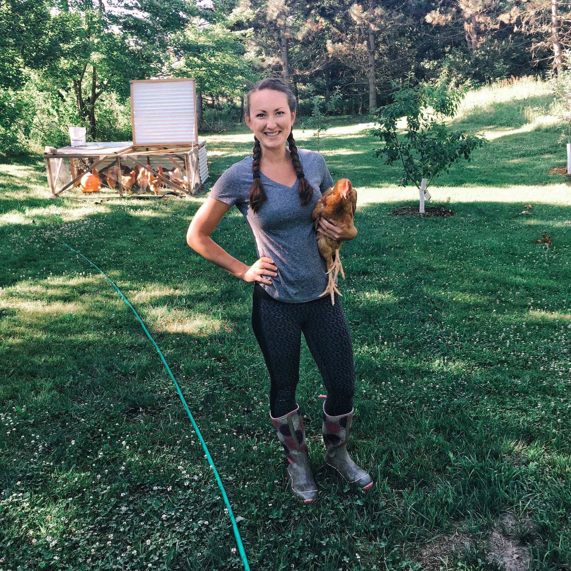 Katie holding a red ranger chicken in front of the chicken tractor