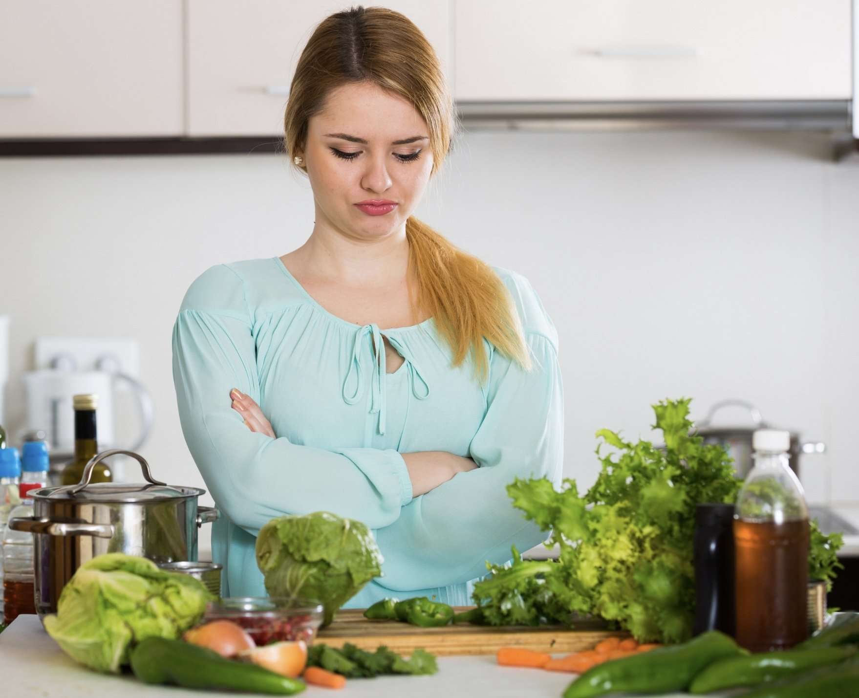 Blonde girl with crossed arms staring at produce on her kitchen counter displeased
