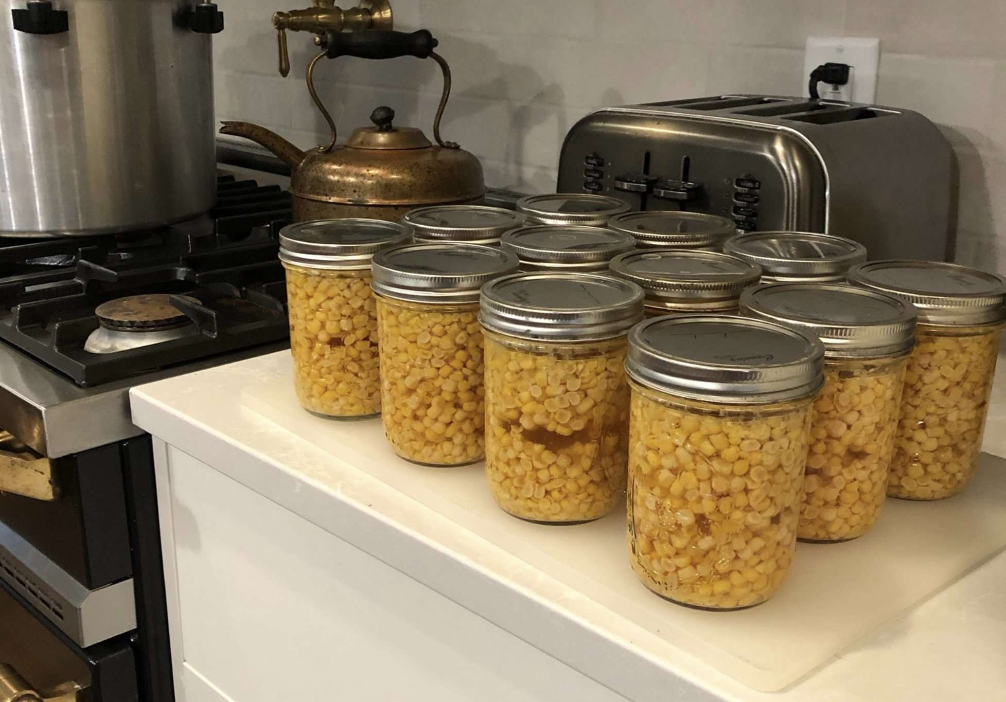 12 jars of pressure canned corn sitting on countertop near stove