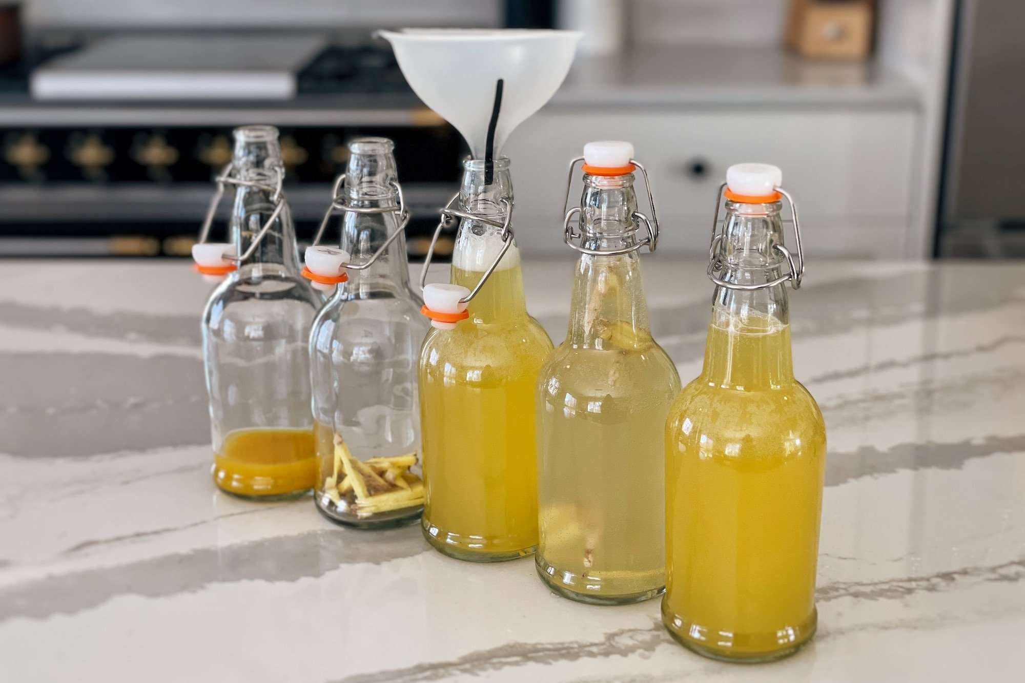 5 glass swing-top bottles being filled with kombucha using a funnel