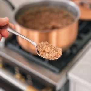 A spoonful of refried beans in front of a copper pot