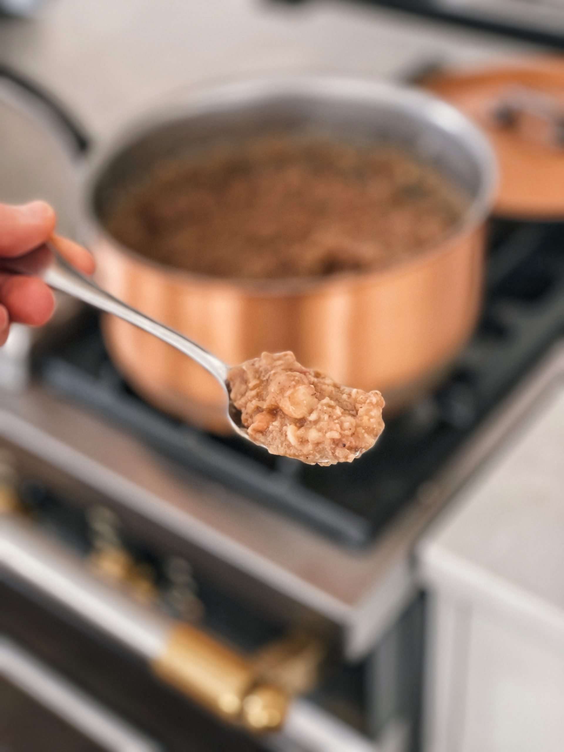 A spoonful of refried beans in front of a copper pot