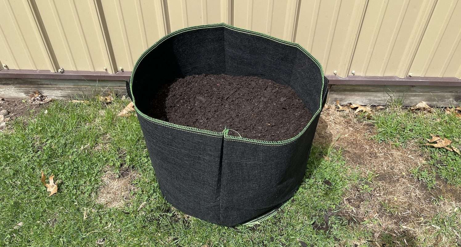 A grow bag halfway filled with potting soil