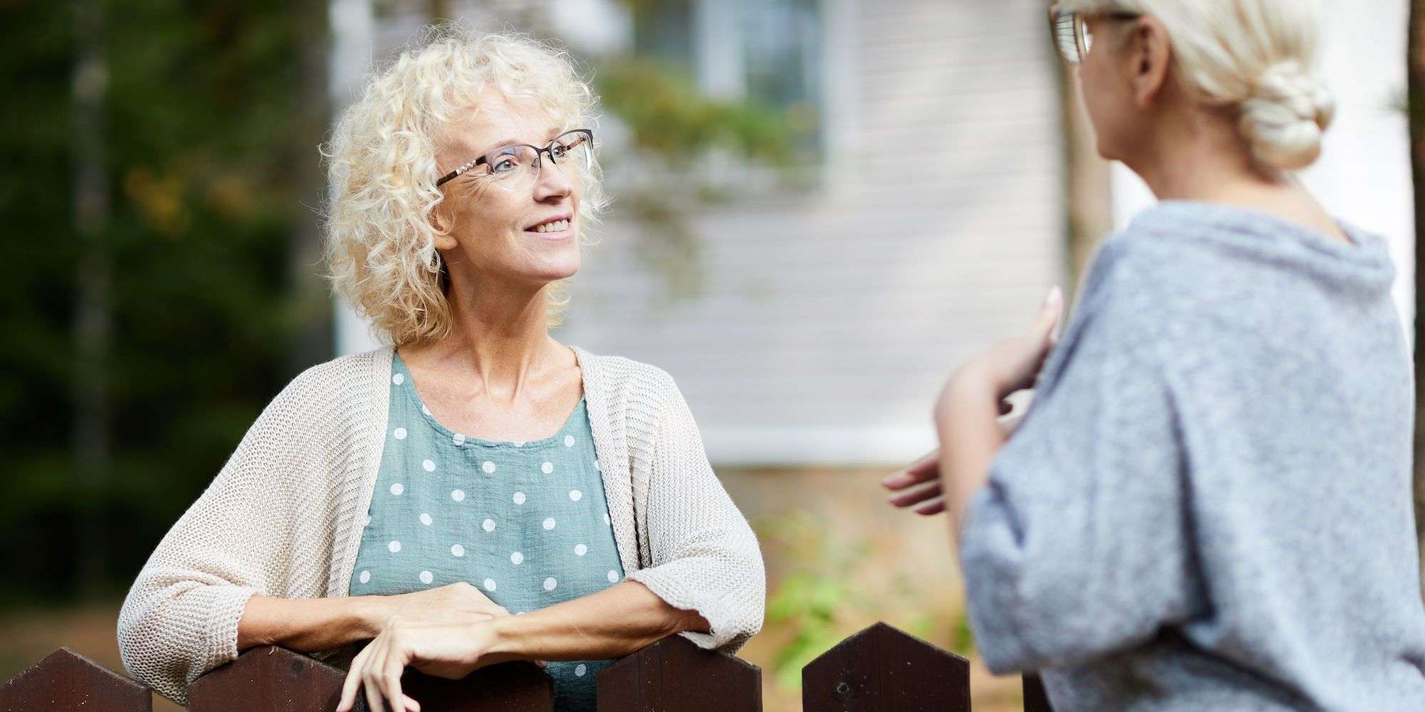 2 neighbors talking over a wooden fence