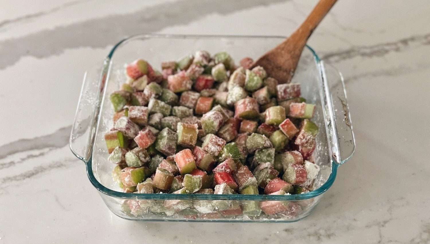 Chopped rhubarb mixed with sugar and flour in a square baking dish