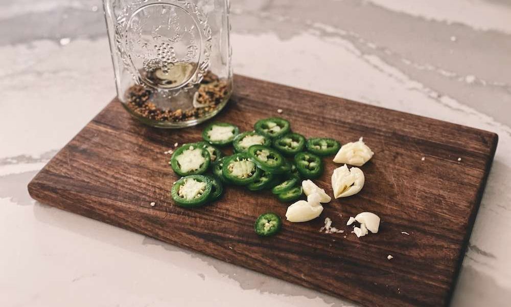 Sliced jalapenos and garlic on a wooden cutting board next to a mason jar