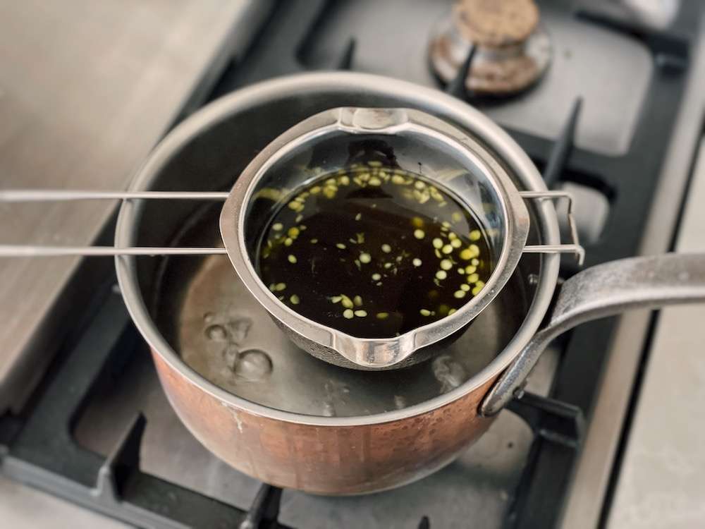 A double boiler set up with the chickweed oil and floating beeswax circles