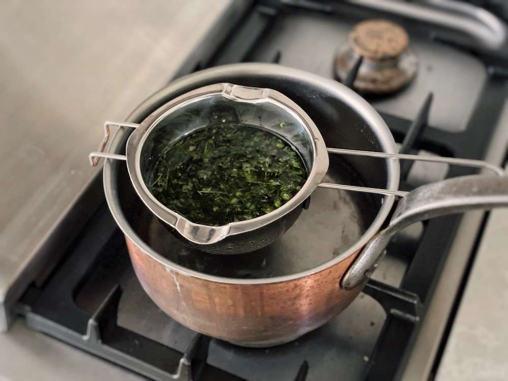 A double boiler set up with chickweed infusing into olive oil