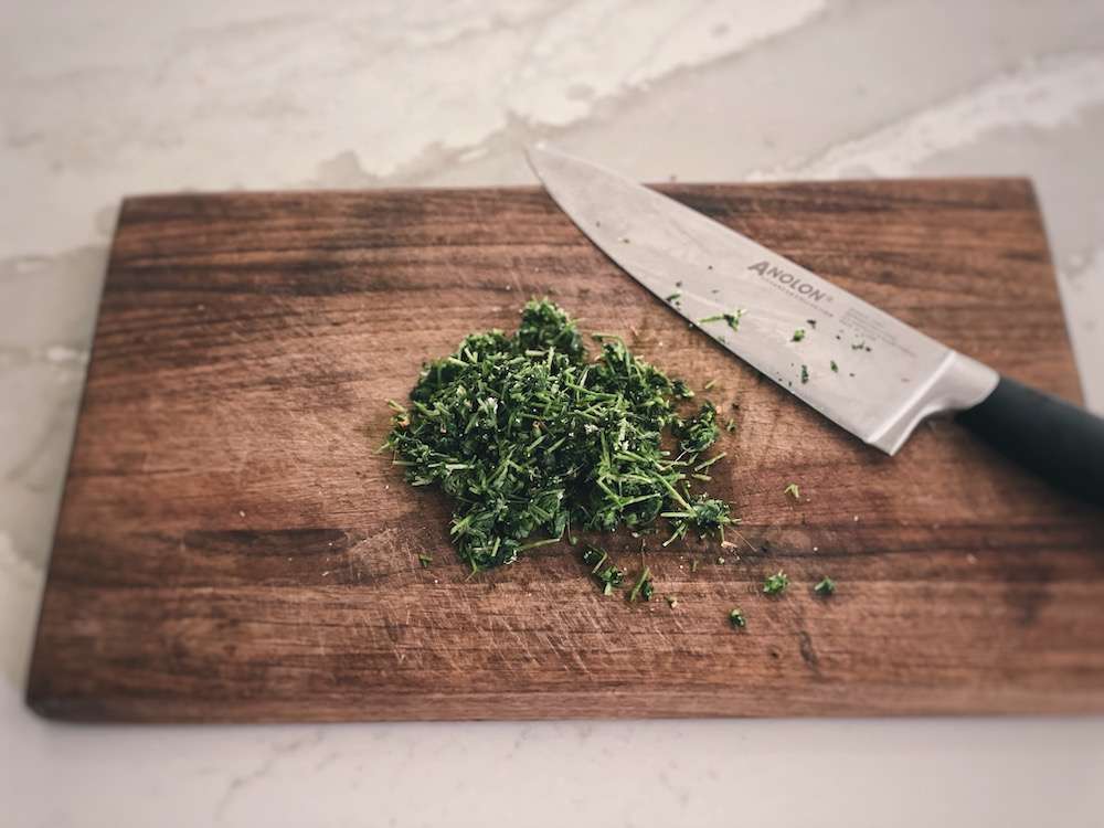 A pile of wilted chickweed on a wood cutting board, freshly chopped with a knife nearby