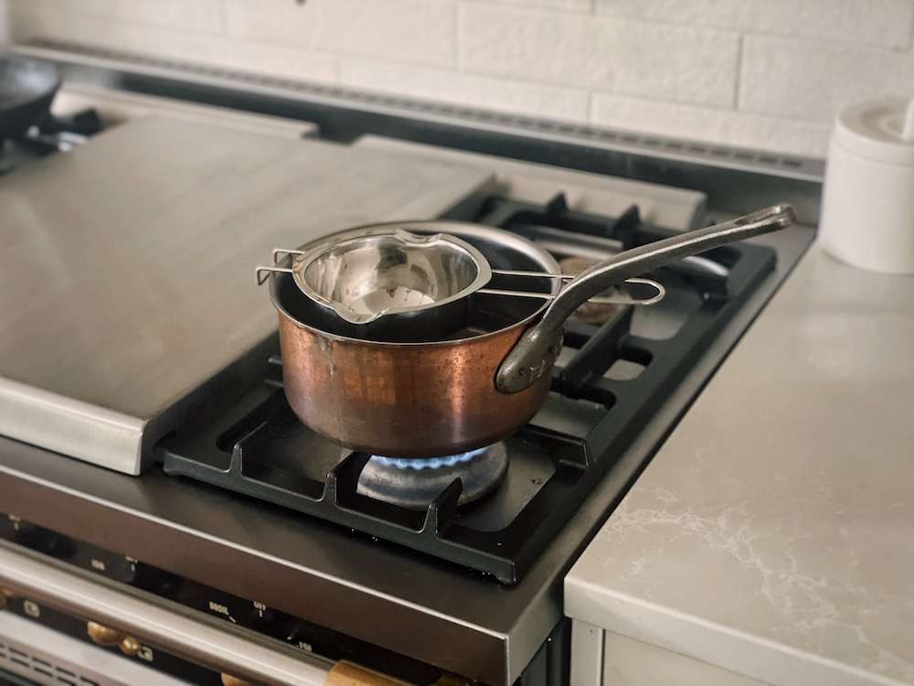 A double boiler insert is set on a copper pot of boiling water