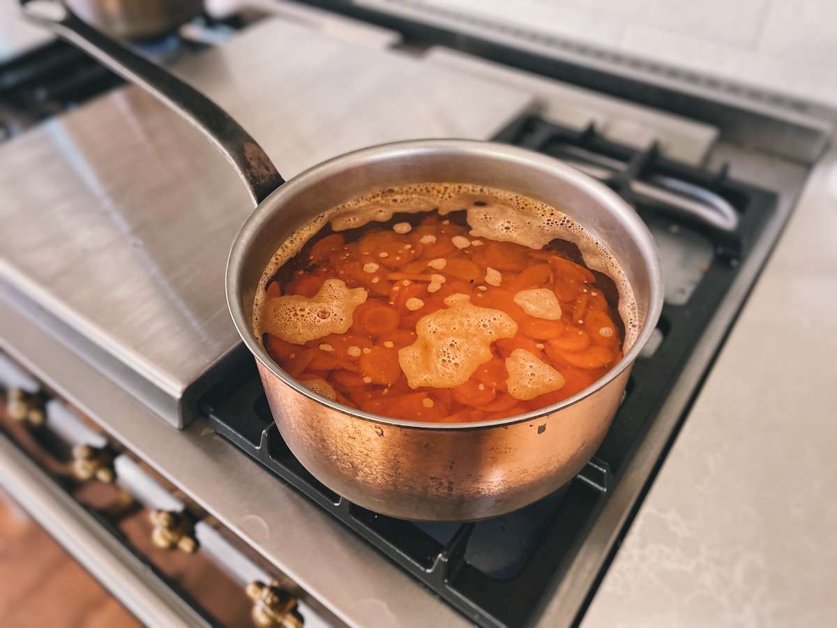 Carrot coins boiling in a copper pot on the stove