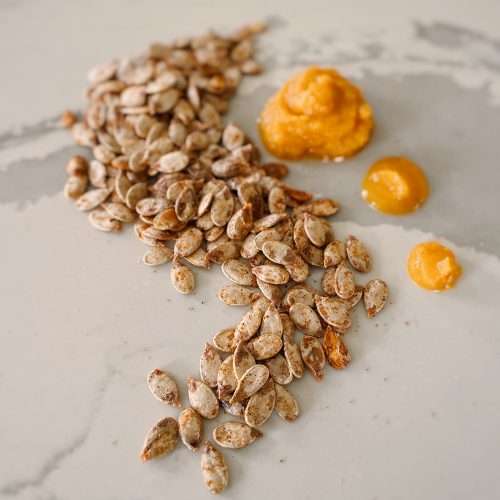 Pumpkin seeds laid out on a kitchen island in a swirl pattern with 3 dots of pureed pumpkin.