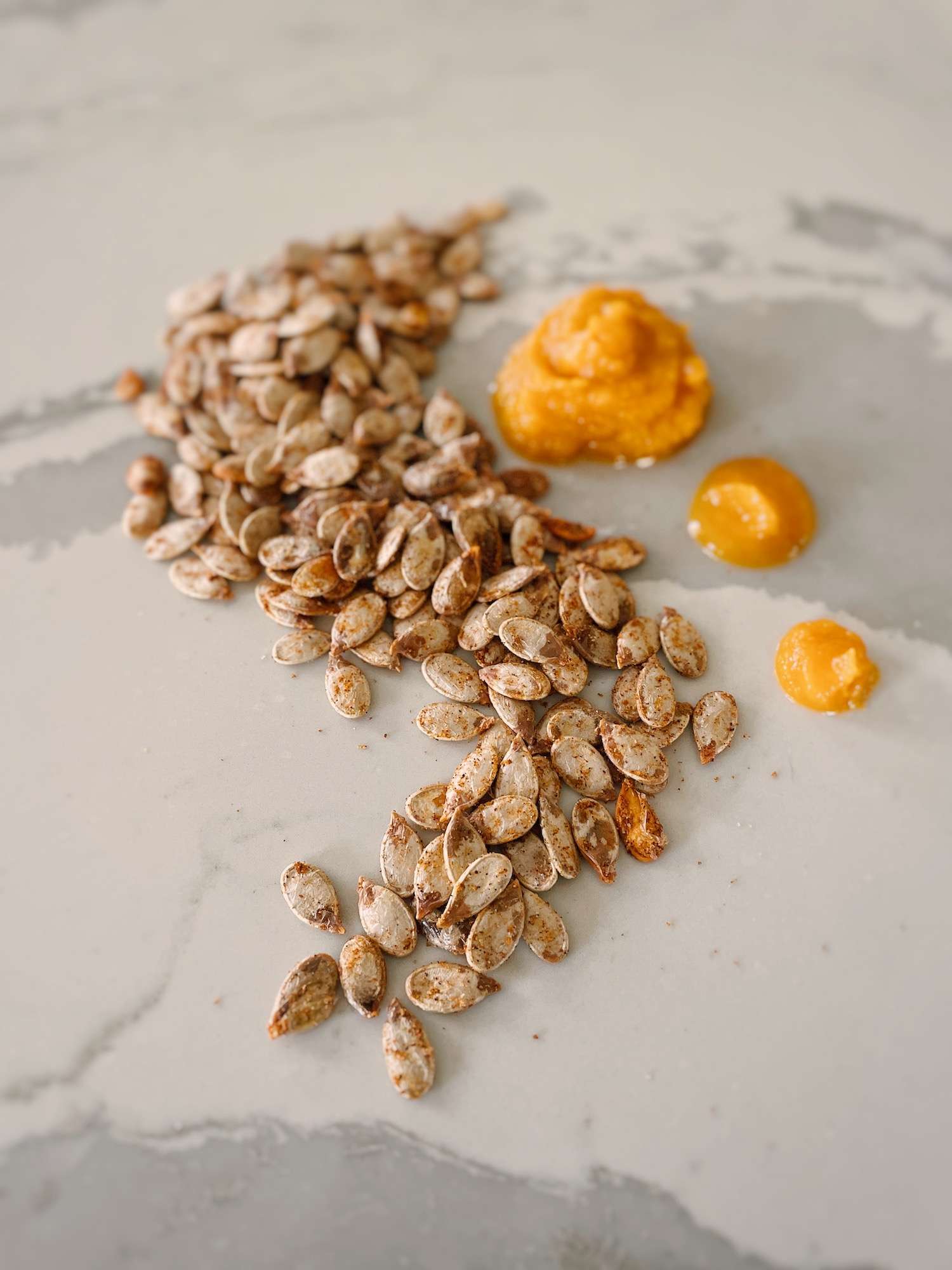 Pumpkin seeds laid out on a kitchen island in a swirl pattern with 3 dots of pureed pumpkin.