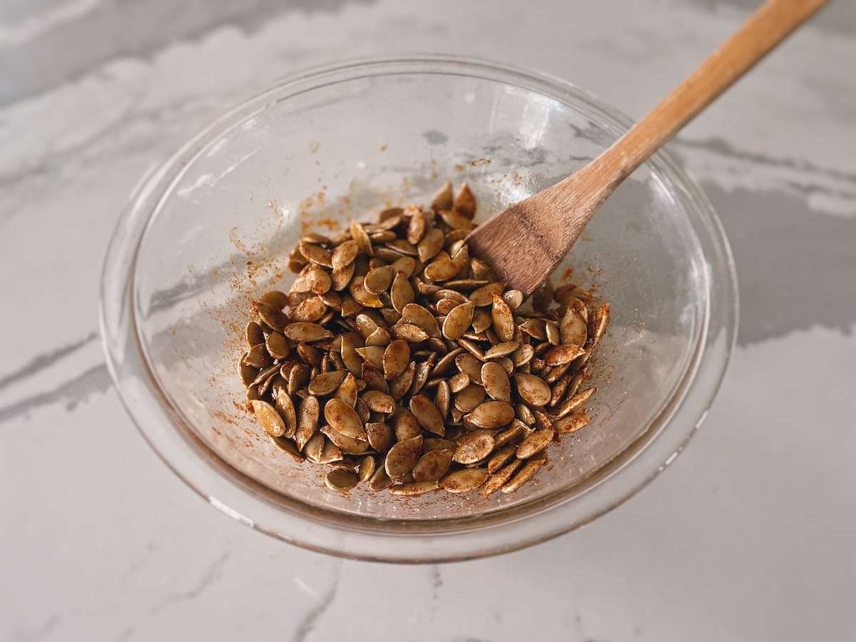 Pumpkin seeds in a glass bowl, tossed with olive oil and spices