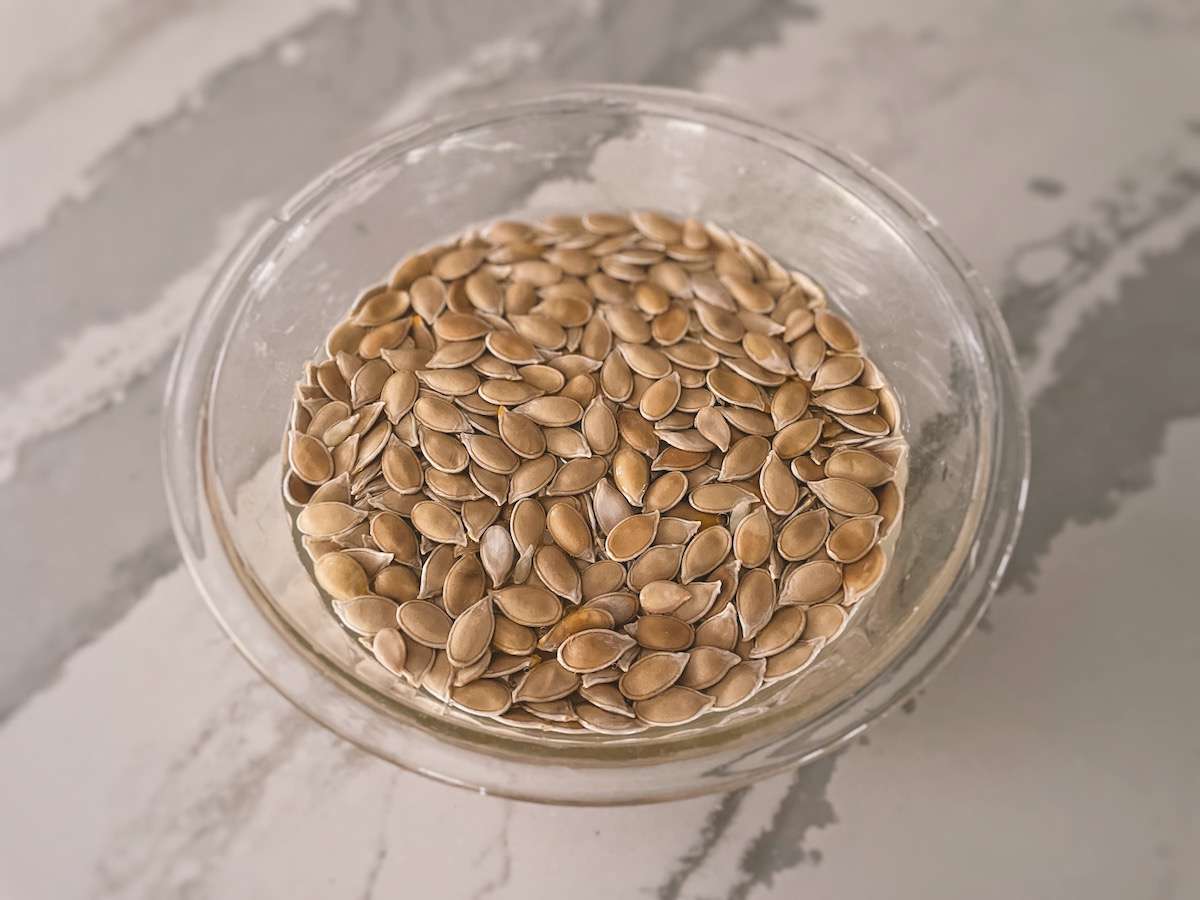 Pumpkin seeds in a glass bowl of water on a kitchen counter