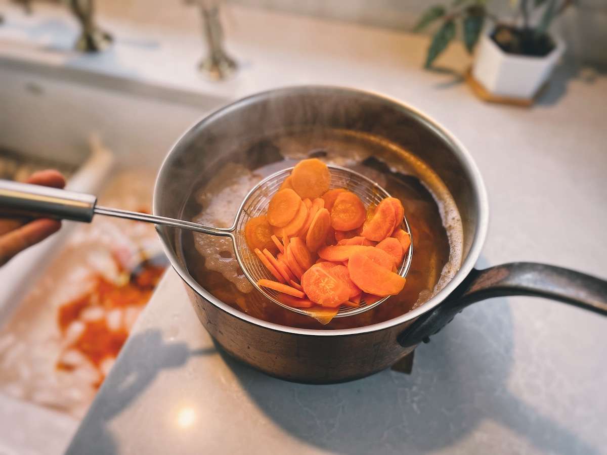 Straining out the carrots using a spider strainer next to the kitchen sink set up as an ice bath