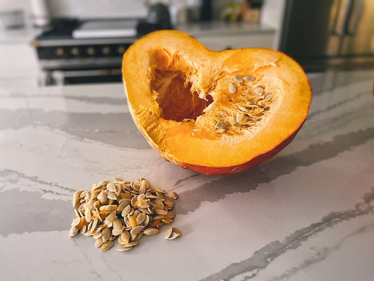 Fresh pumpkin seeds sitting on a kitchen island in front of a whole half of a pumpkin