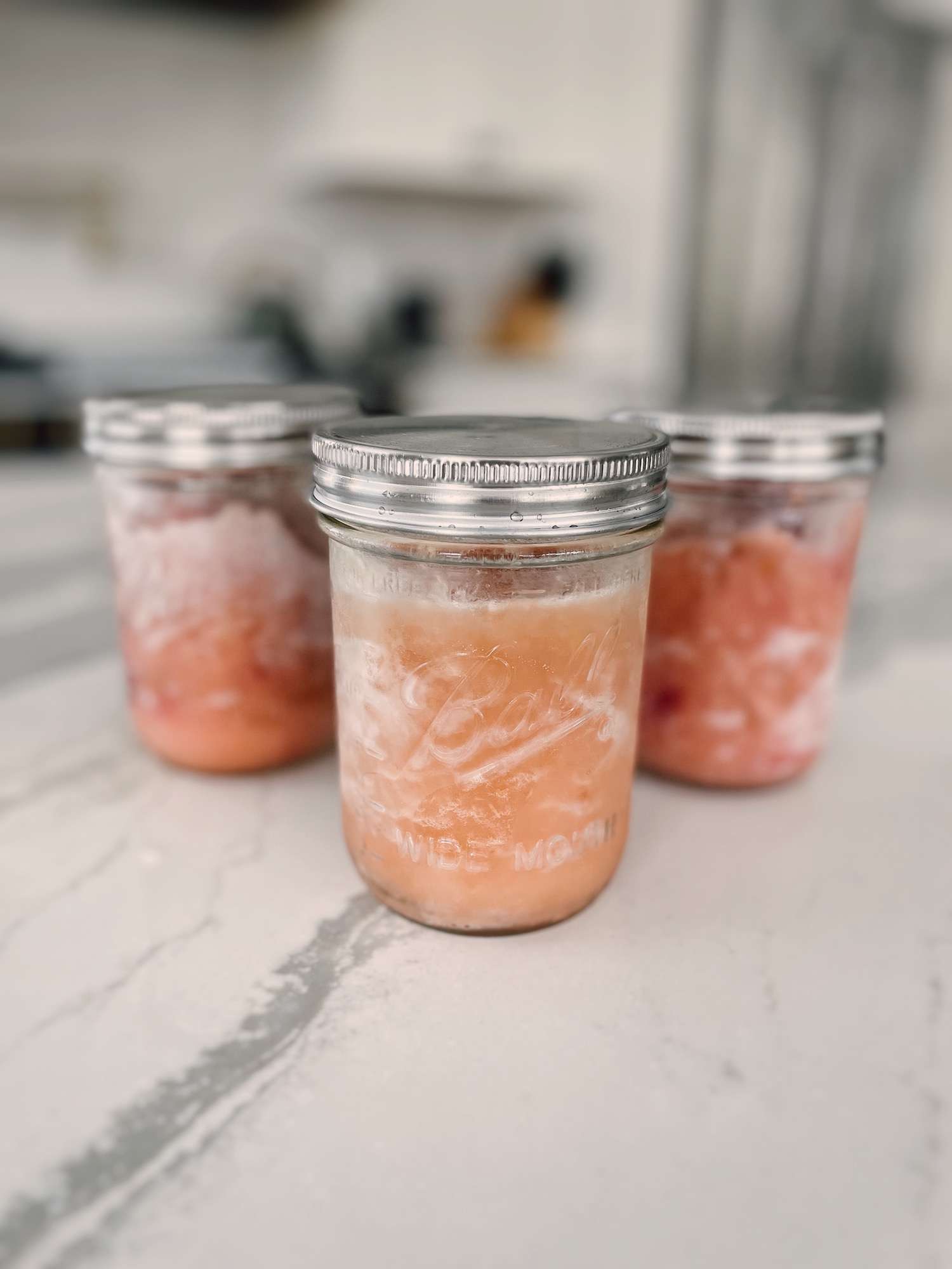 3 mason jars filled with frozen applesauce sitting on a kitchen island