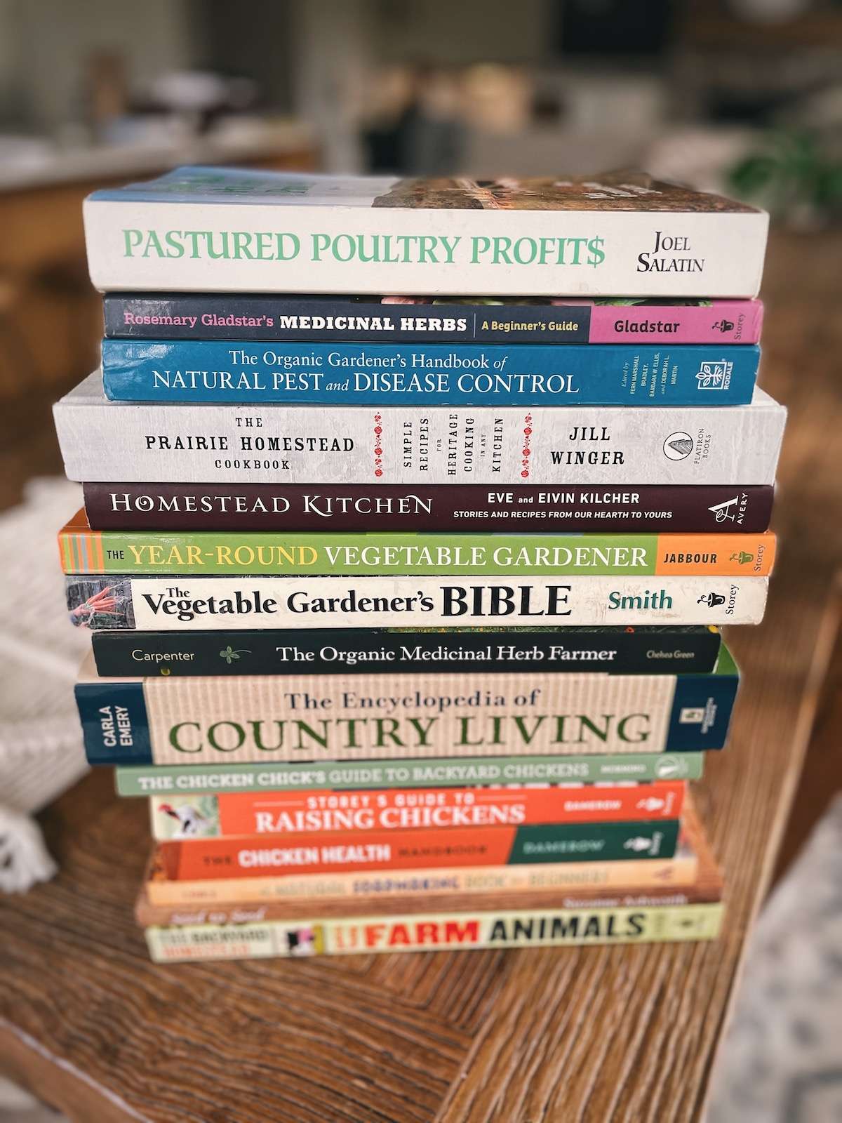 A stack of the best homesteading books on a wooden kitchen table