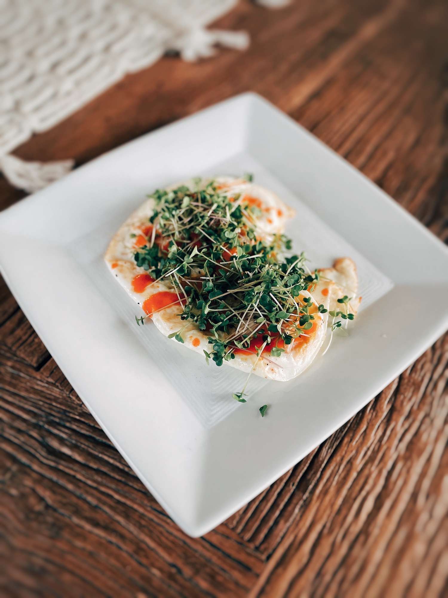 Broccoli microgreens piled on top of a white plate of over-easy eggs