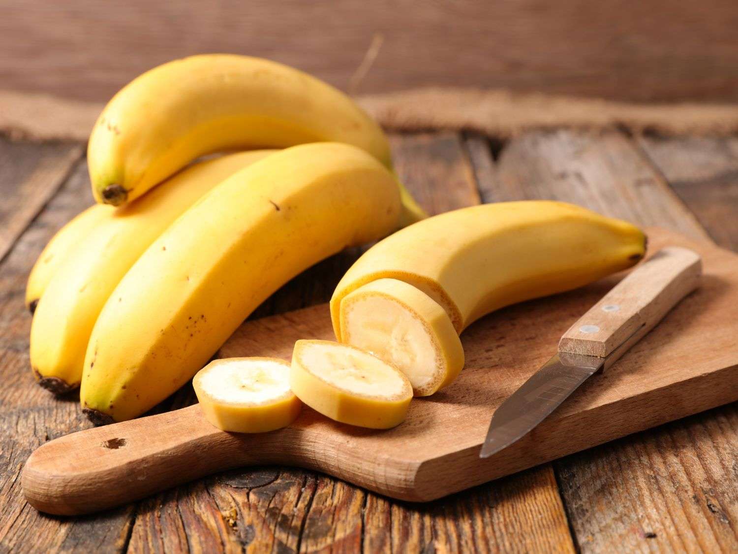 A photo of bananas being sliced on a wooden cutting board