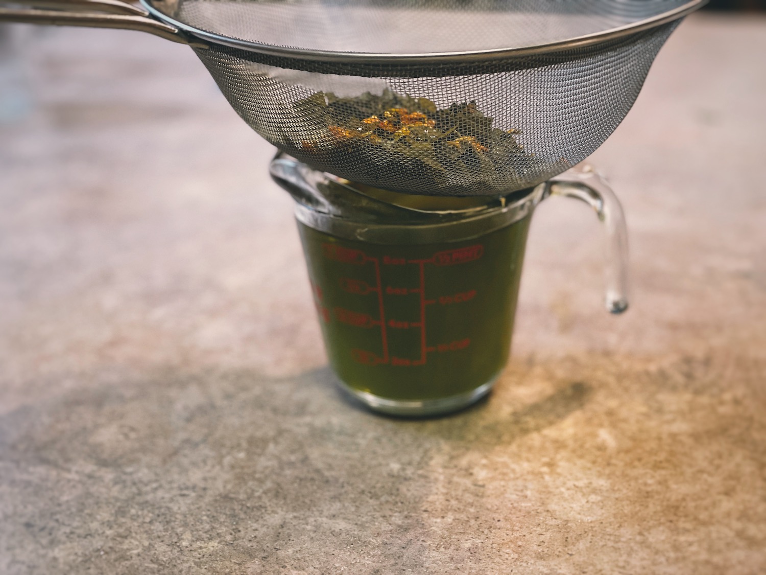 A glass measuring cup with the infused oil with strained herbs on top