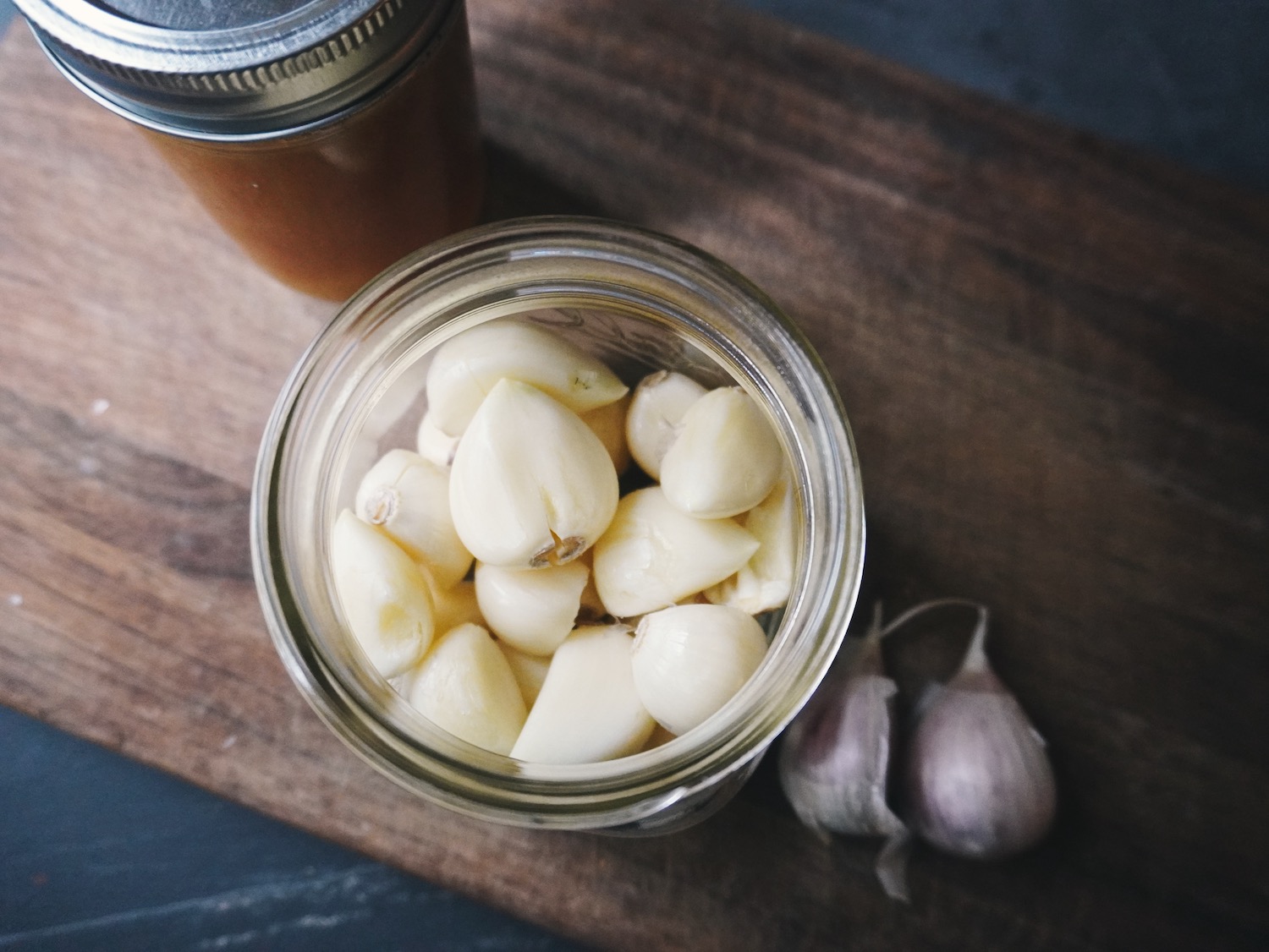 A glass jar filled with peeled garlic cloves sitting on a wooden cutting board
