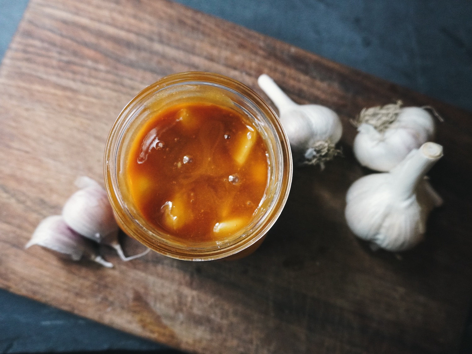 fermented honey garlic in a jar sitting on a wooden cutting board.