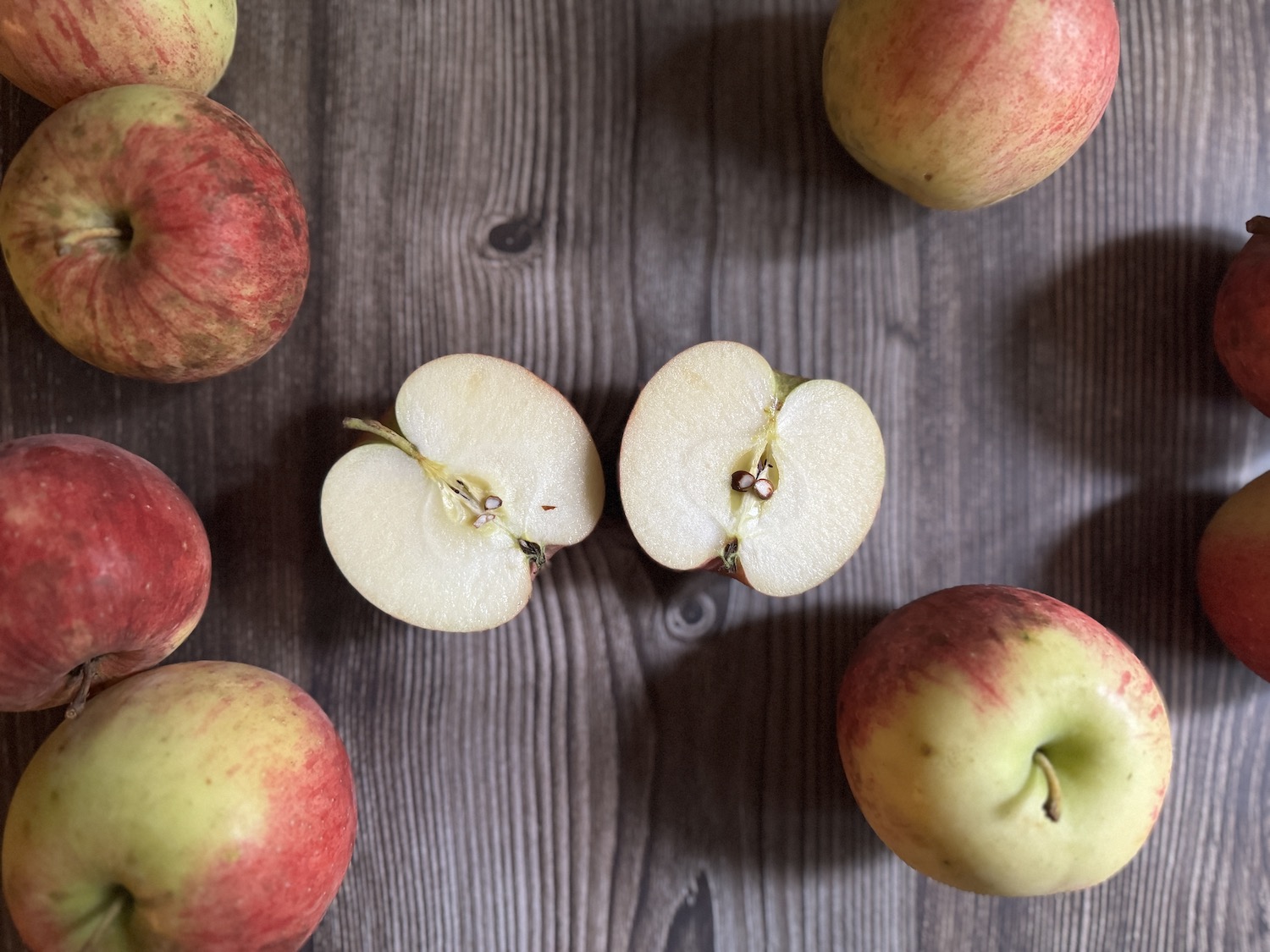 A photo of a cut apple laying on a wooden cutting board and surrounded by whole apples