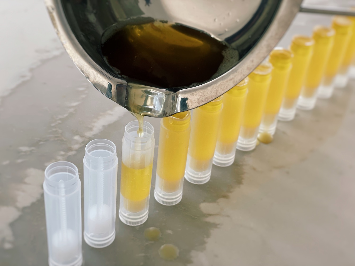 A photo showing melted lip balm being poured into tubes using a double boiler