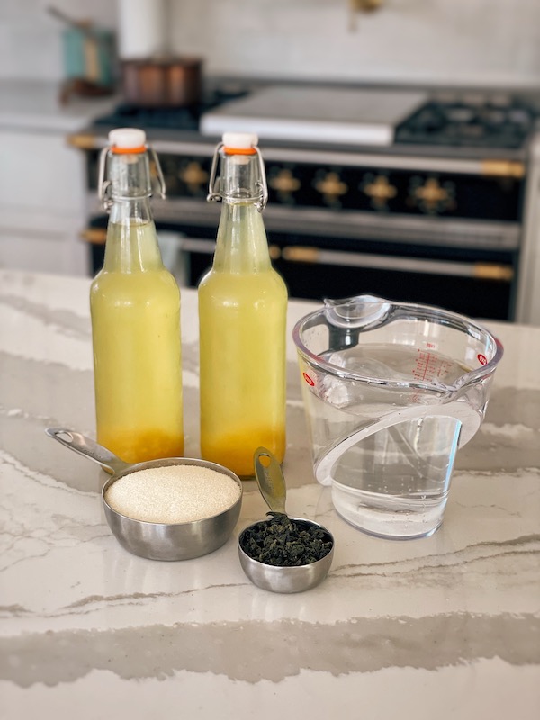 A photo showing kombucha bottles next to ingredients on a kitchen island