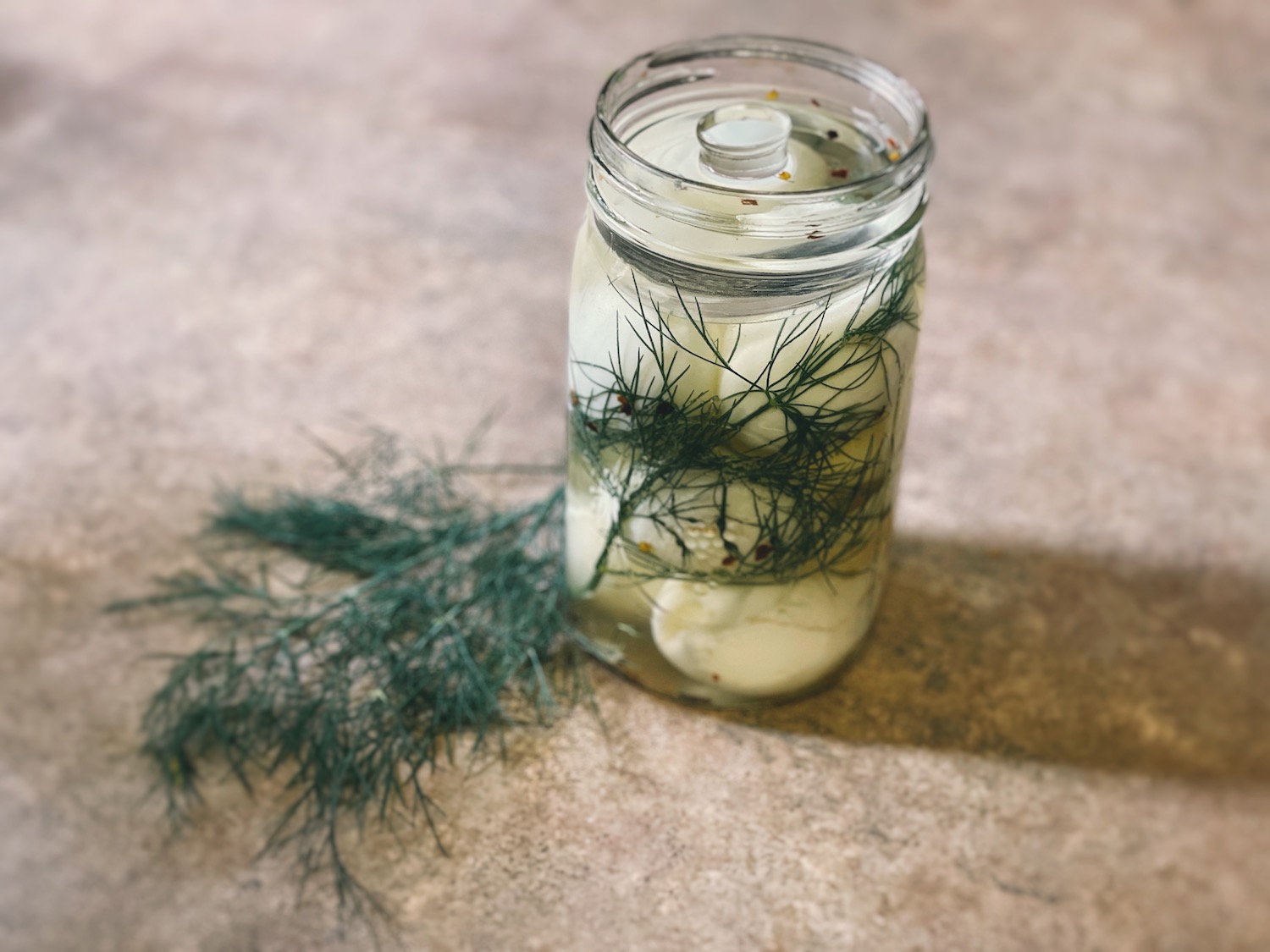 Fermented eggs in a glass quart mason jar with a sprig of dill next to it.