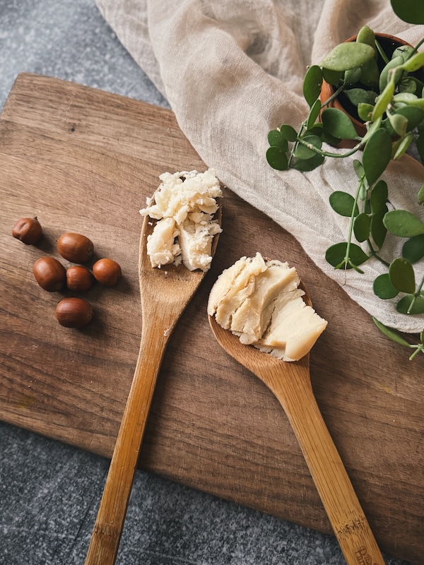 A wooden spoonful of lard and a spoonful of tallow sitting on a wooden cuttingboard with acorns, cheese cloth and some greens