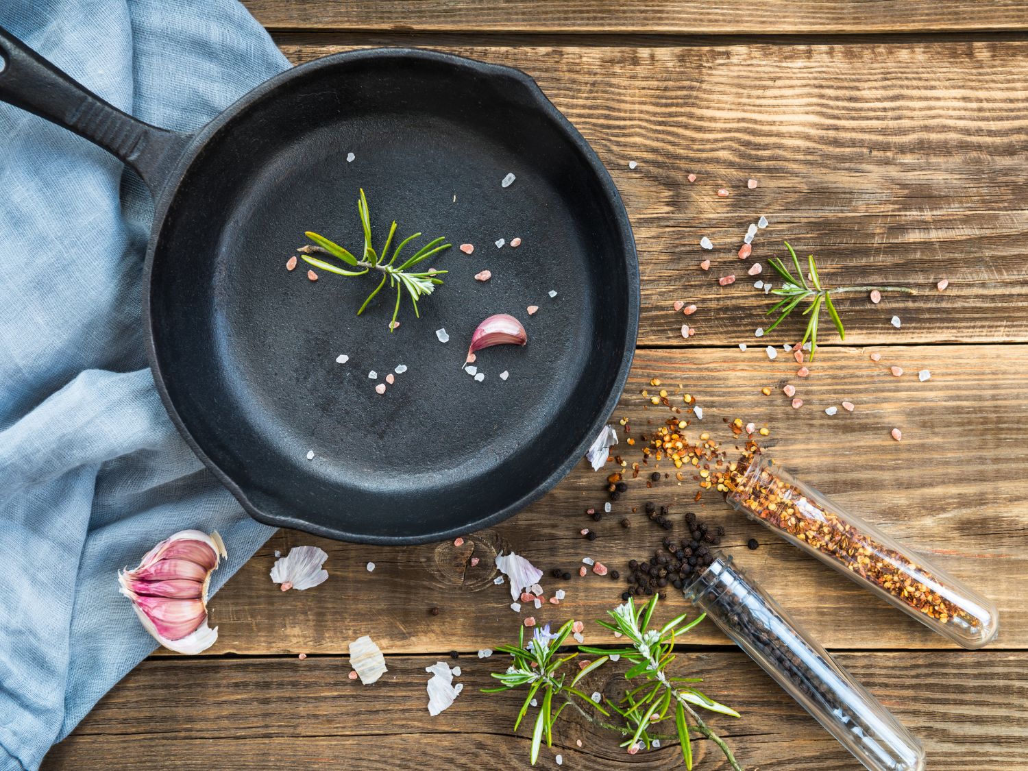 A cast iron skillet is sitting on a wooden background with a blue towel and some herbs