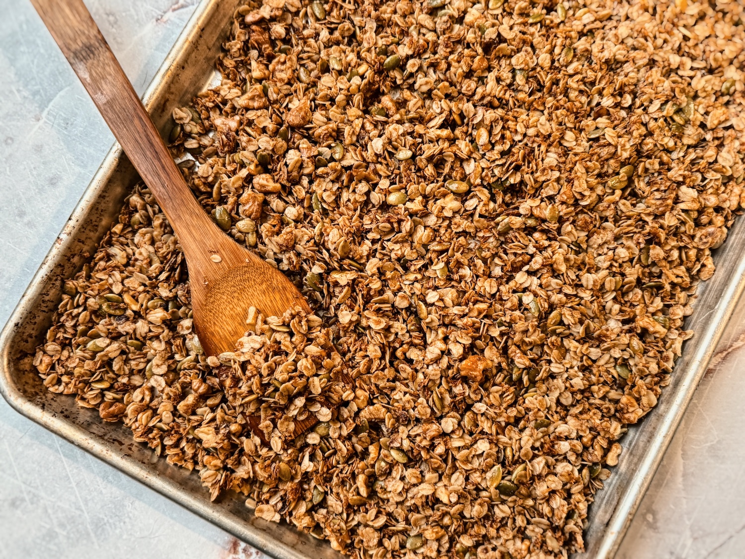 Finished homemade granola on a sheet pan with a wooden spoon
