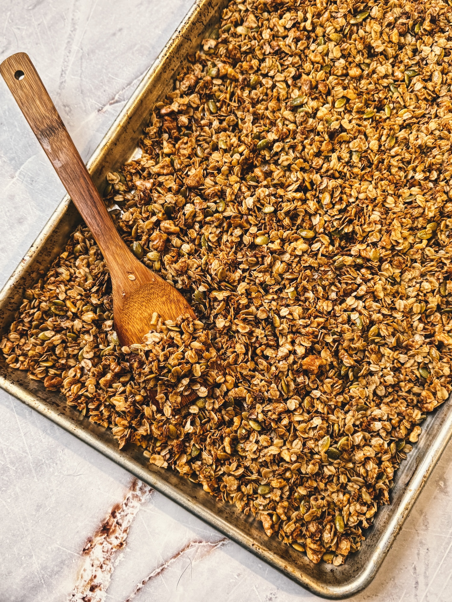 Finished homemade granola on a sheet pan with a wooden spoon