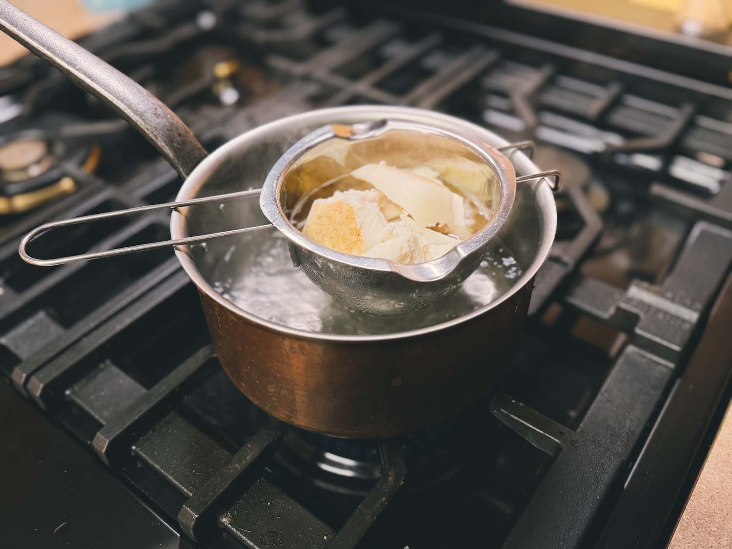 A stainless steel double boiler nestled in a small pot with melting tallow inside.