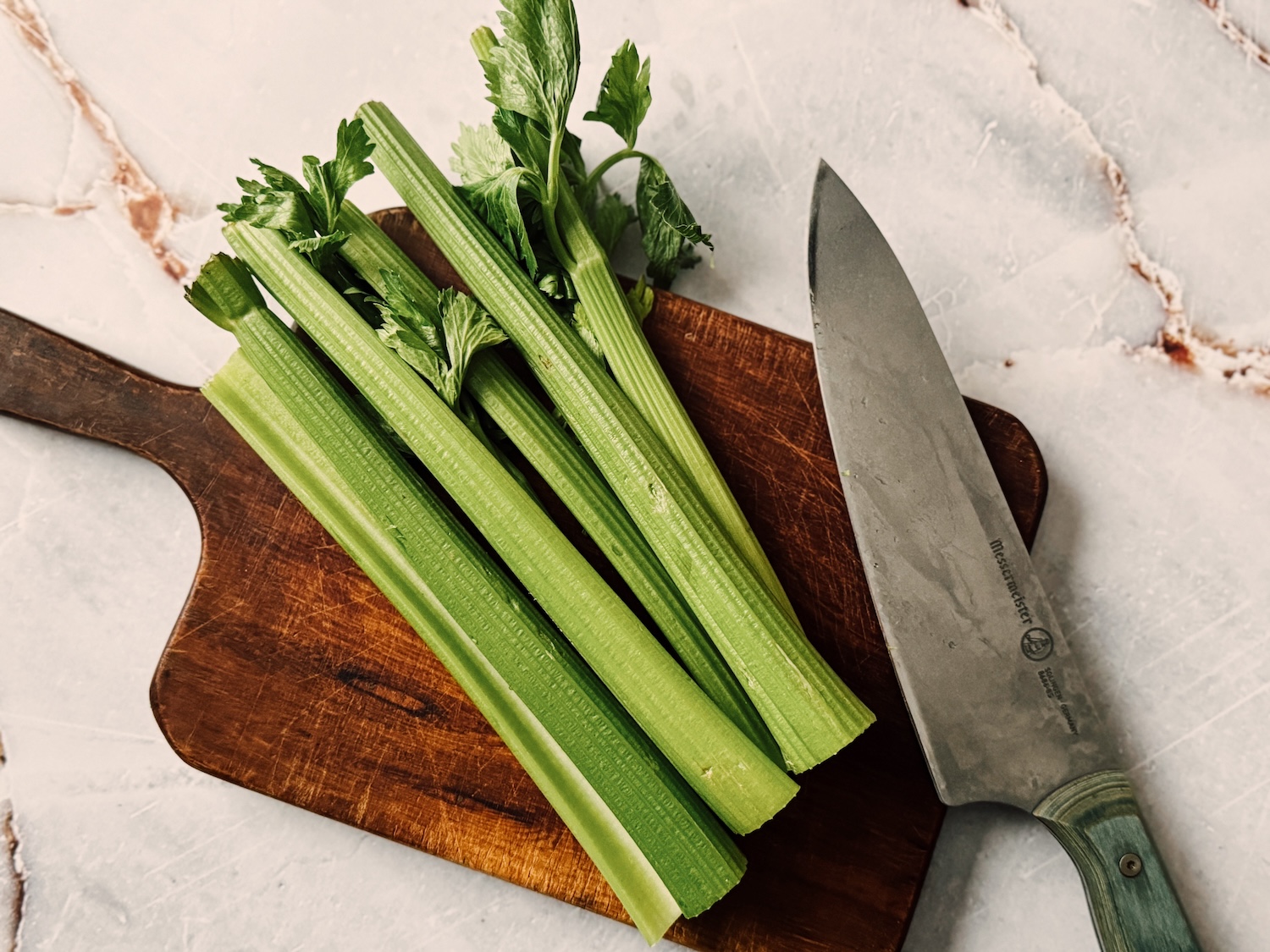 Celery stalks laid out on a wooden cutting board with a knife next to them. 