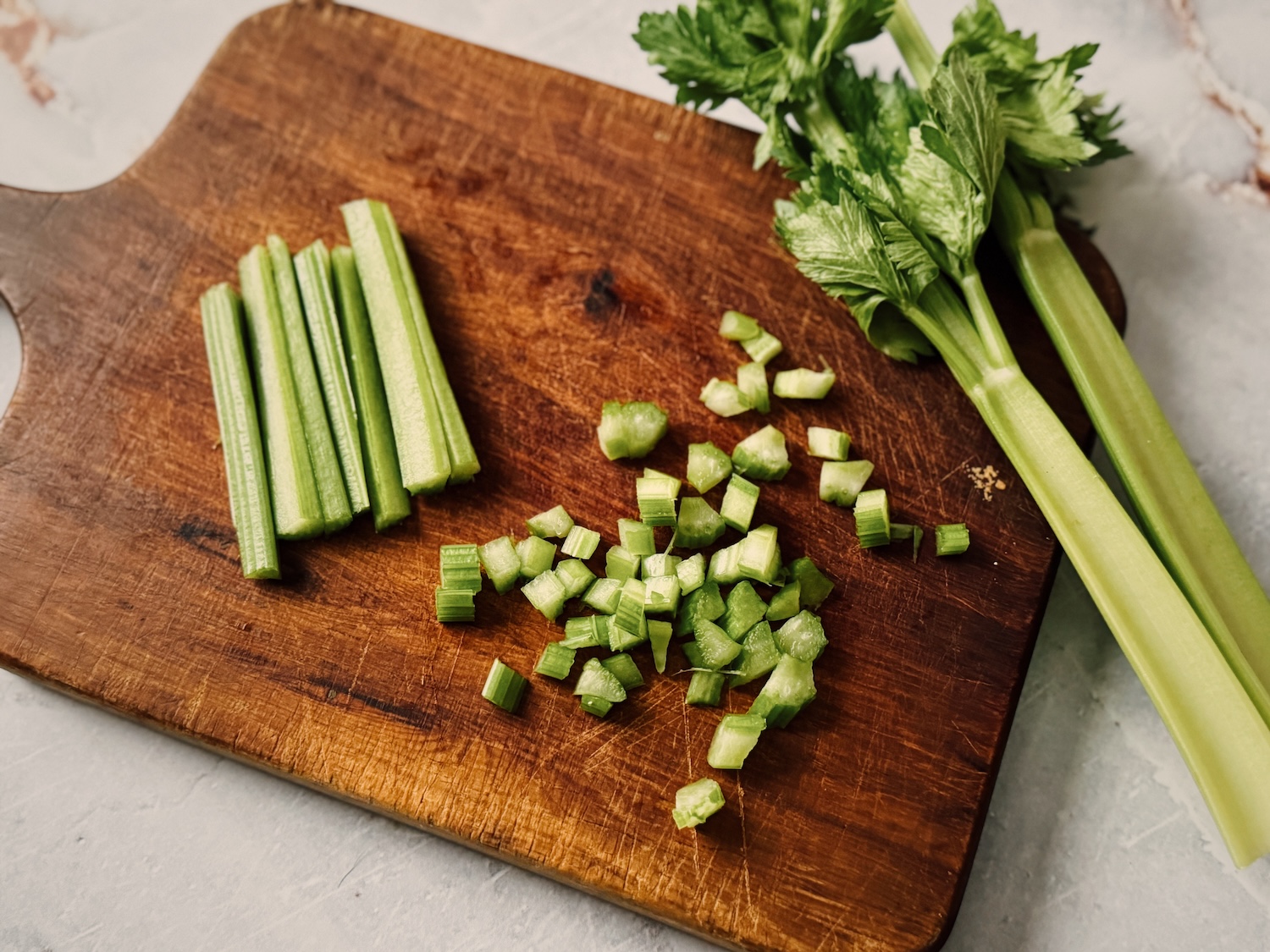 Whole celery stalks, celery strips and celery pieces all on a wooden cutting board.