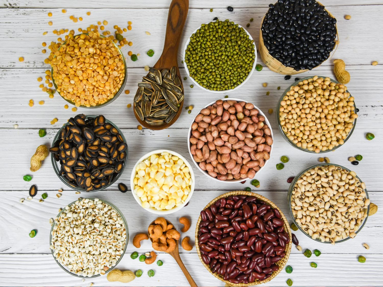 Many small containers filled with different kinds of beans set on a wooden background