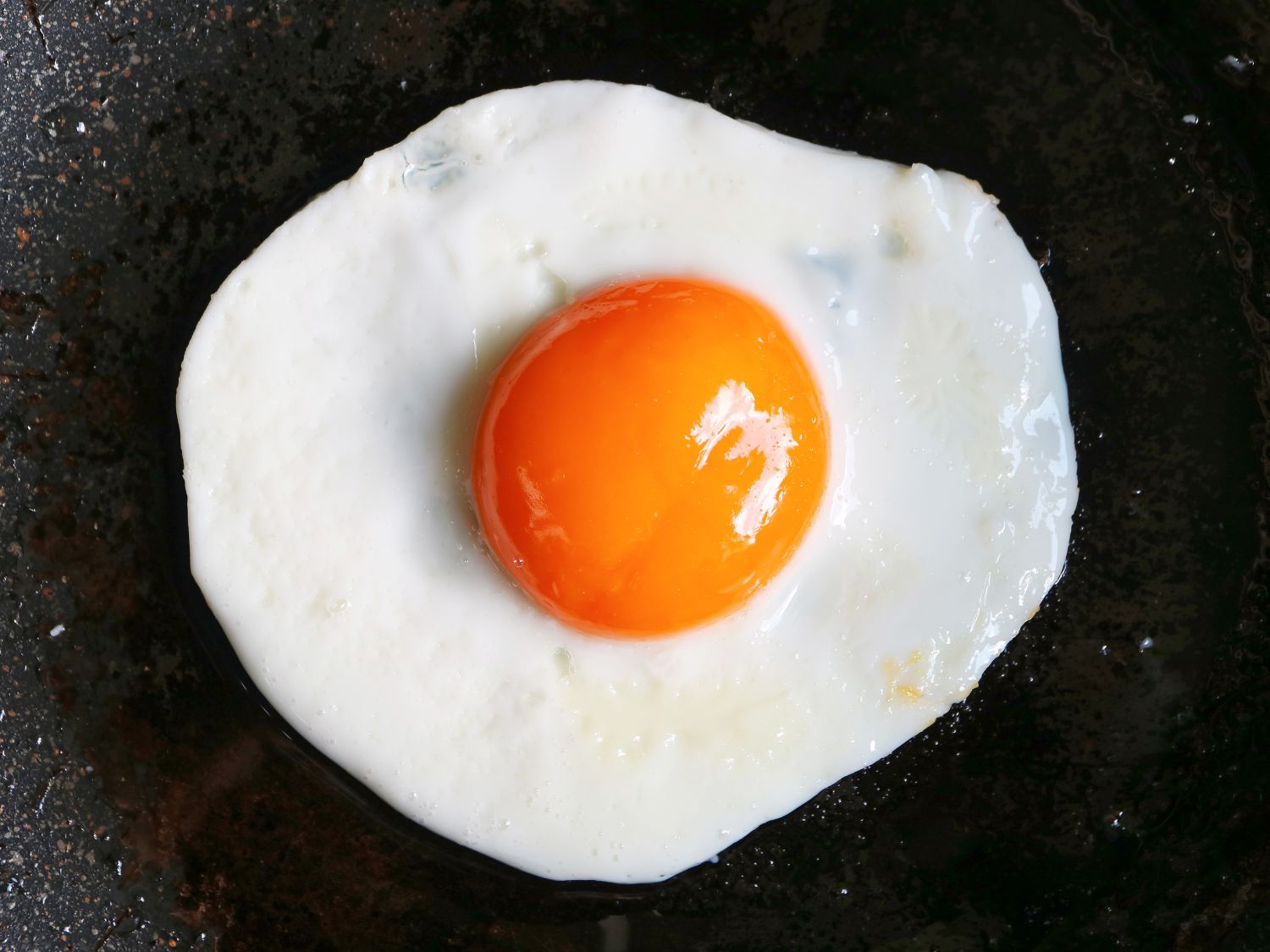 A cracked egg on a dark background. The egg has an orange colored yolk.