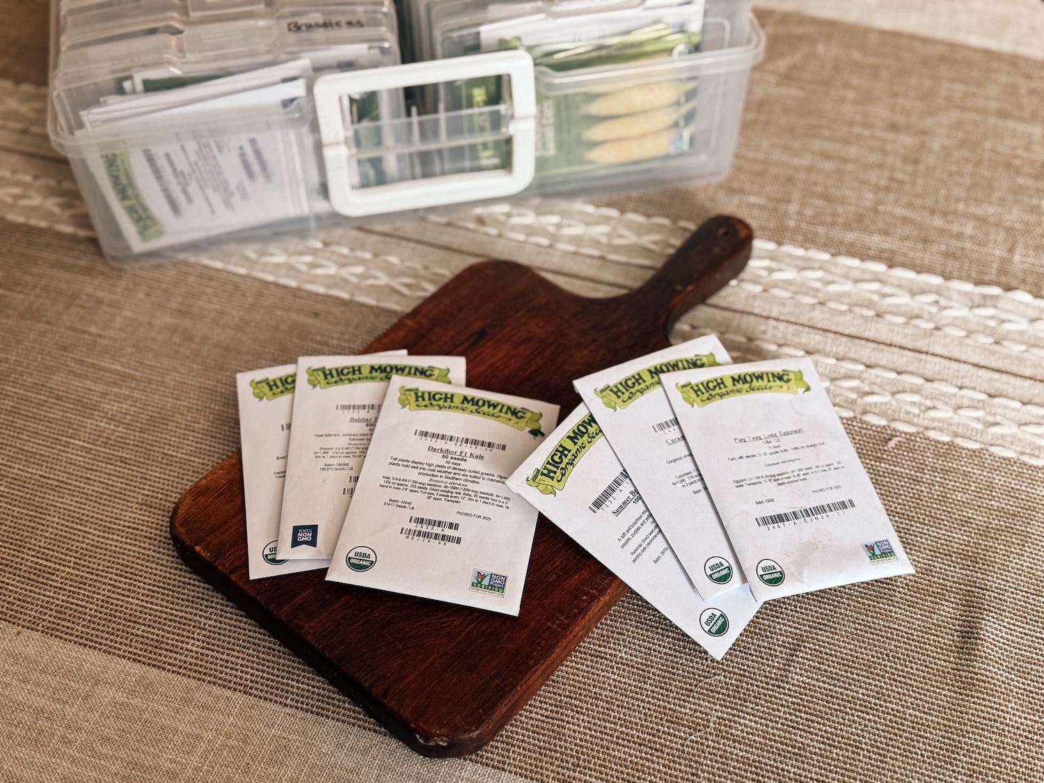 6 packets of seeds are laid out on a wooden cutting board on a kitchen table