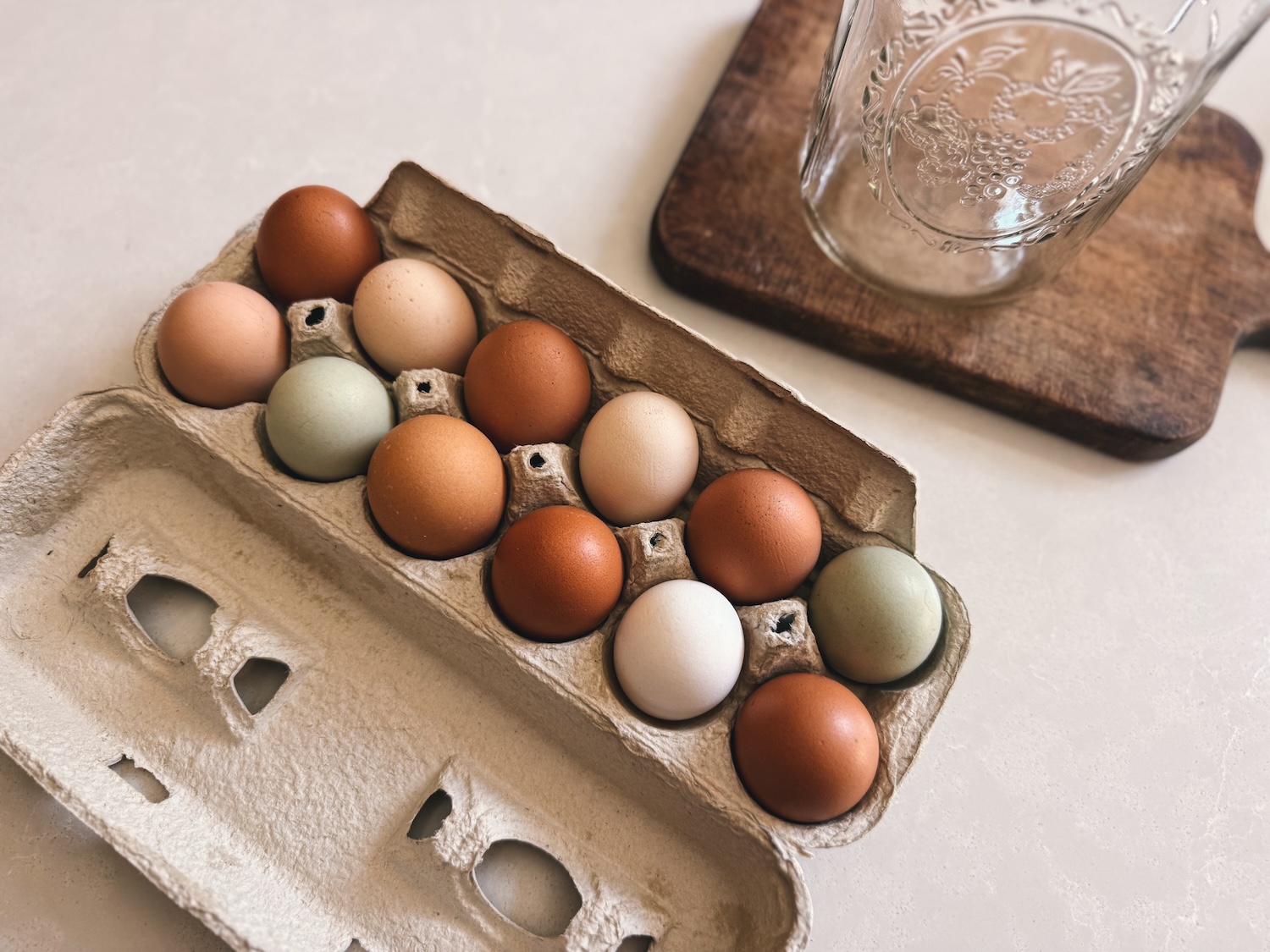 A carton of a dozen eggs sitting out on a kitchen island near a wooden cutting board