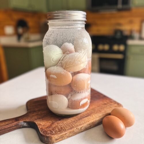 A half gallon glass jar is filled with water glassed eggs and sitting on a wooden cutting board