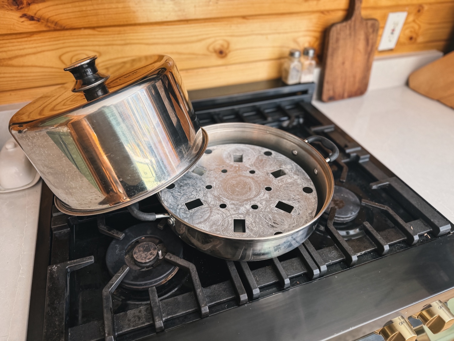 A steam canner is sitting on an oven range with the lid off to the side so the inside of the canner can be seen