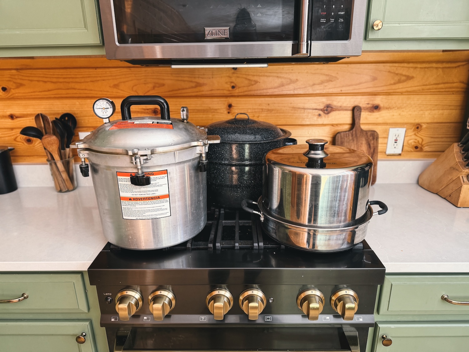 A pressure canner, water bath canner, and steam canner are sitting on a range in a kitchen